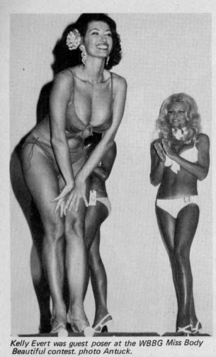 Kellie in Wiiner pose in the WBBG Miss Body Beautifl contest. Kneely over flashes breats and smile next to buffy, buxom blonde in white bikini